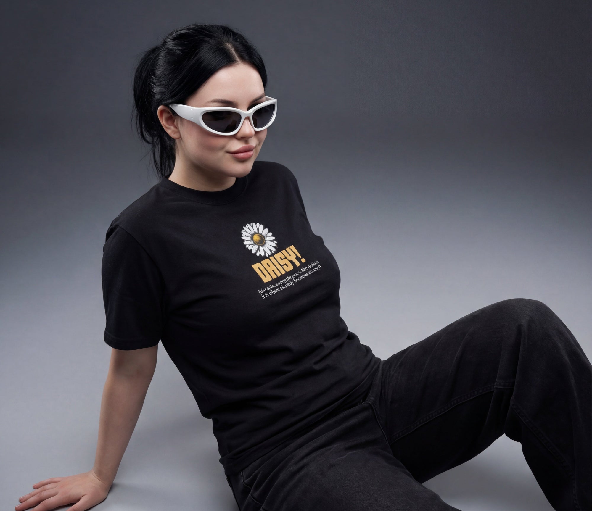 Person wearing a black t-shirt with DESIGN OF DAISY, sitting on a gray background